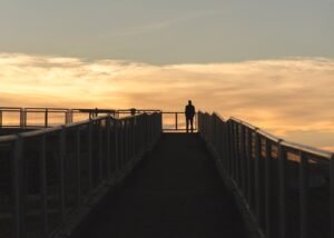 silhouette photography of man standing on corner of bridge